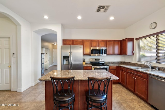 kitchen with a kitchen breakfast bar, stainless steel appliances, sink, stone counters, and a center island