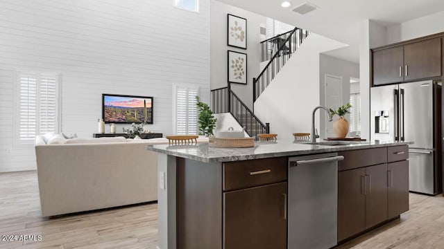 kitchen with a center island with sink, dark brown cabinets, stainless steel appliances, and light hardwood / wood-style flooring