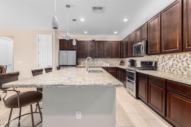 kitchen featuring dark brown cabinetry, pendant lighting, sink, stainless steel appliances, and a breakfast bar area