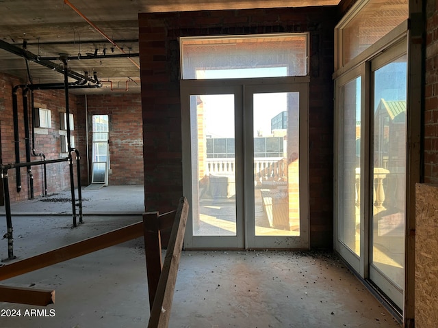 entryway featuring plenty of natural light, french doors, brick wall, and concrete floors