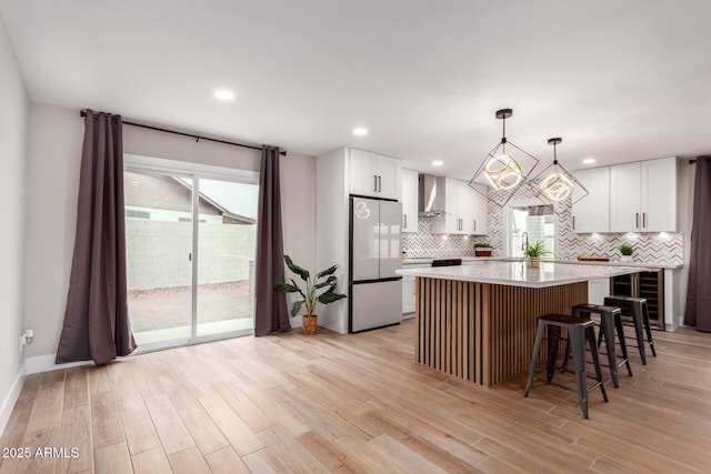 kitchen with light wood finished floors, wall chimney exhaust hood, a center island, and freestanding refrigerator