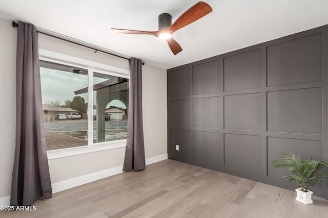 empty room featuring baseboards, light wood finished floors, a ceiling fan, and a decorative wall