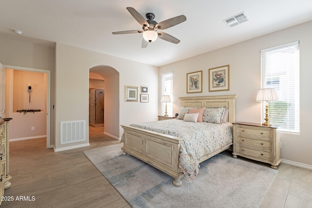 bedroom with light wood-type flooring, arched walkways, visible vents, and baseboards