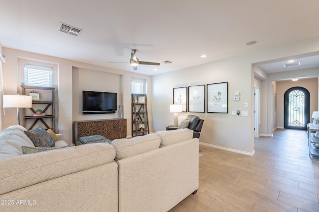 living area featuring arched walkways, visible vents, ceiling fan, and baseboards