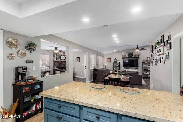 kitchen with blue cabinets, ceiling fan, light stone counters, and a fireplace