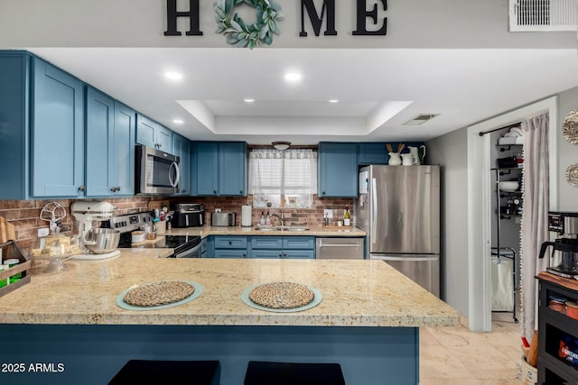 kitchen featuring sink, a tray ceiling, stainless steel appliances, and kitchen peninsula