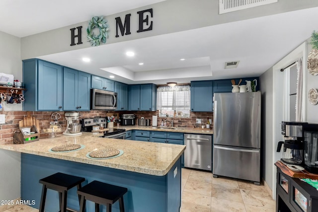 kitchen featuring appliances with stainless steel finishes, a raised ceiling, kitchen peninsula, and blue cabinets