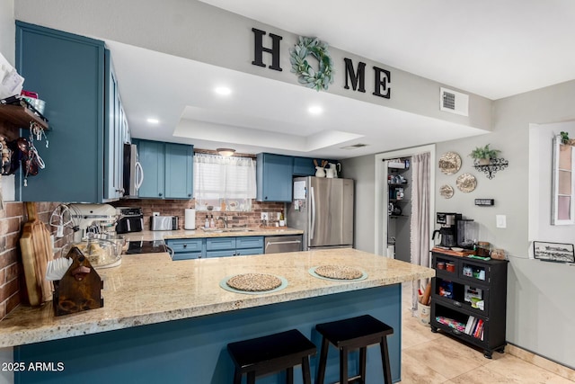 kitchen featuring a kitchen bar, blue cabinets, a raised ceiling, kitchen peninsula, and stainless steel appliances