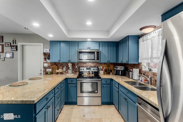 kitchen with a tray ceiling, sink, kitchen peninsula, stainless steel appliances, and light stone countertops