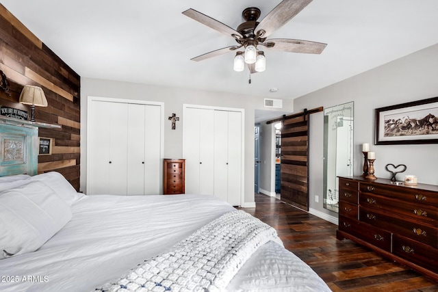 bedroom with ceiling fan, dark hardwood / wood-style floors, a barn door, and multiple closets