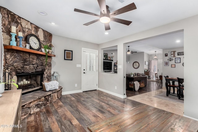 living room featuring wood-type flooring, a stone fireplace, and ceiling fan