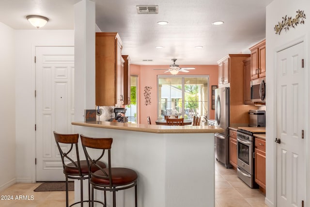 kitchen with a breakfast bar area, kitchen peninsula, light tile patterned floors, appliances with stainless steel finishes, and ceiling fan