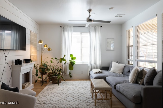 living area with light wood-type flooring, a fireplace, visible vents, and a ceiling fan