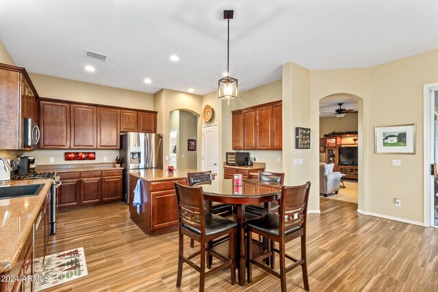 kitchen featuring a center island, decorative light fixtures, light hardwood / wood-style floors, light stone counters, and stainless steel appliances