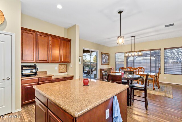 kitchen featuring a center island, light stone countertops, wood-type flooring, and hanging light fixtures