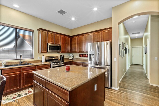 kitchen featuring light stone countertops, appliances with stainless steel finishes, sink, light hardwood / wood-style floors, and a kitchen island