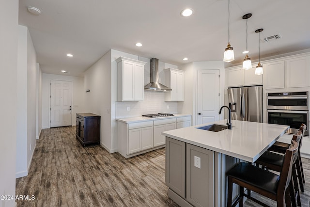 kitchen with stainless steel appliances, sink, wall chimney range hood, a center island with sink, and white cabinetry