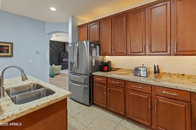 kitchen featuring brown cabinets, light stone counters, a sink, and stainless steel fridge with ice dispenser