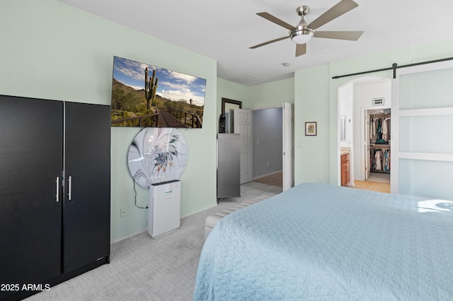 bedroom with a ceiling fan, light carpet, and a barn door