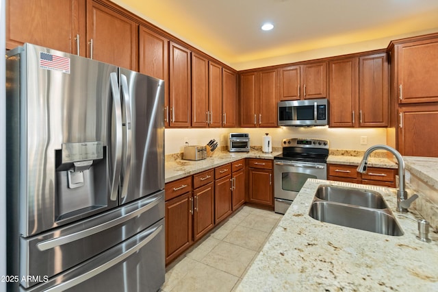 kitchen with light tile patterned floors, light stone counters, stainless steel appliances, a sink, and brown cabinetry