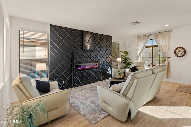 living area with an accent wall, light wood-type flooring, a fireplace, and visible vents