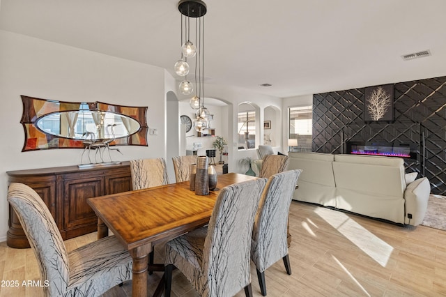 dining space featuring arched walkways, an accent wall, visible vents, light wood-style floors, and a glass covered fireplace