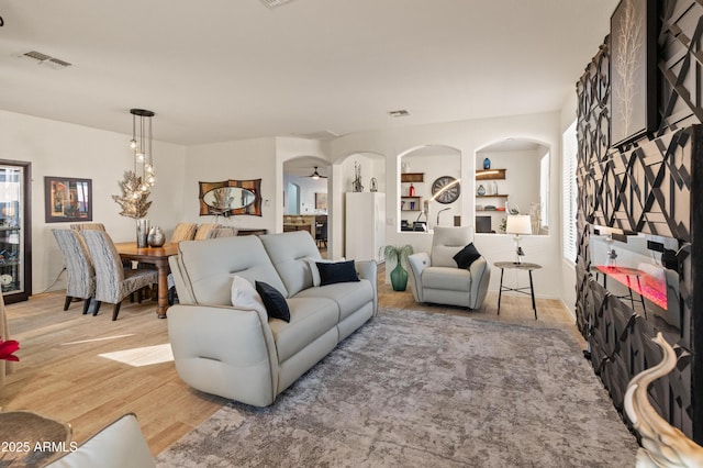 living area with arched walkways, light wood-type flooring, visible vents, and built in features