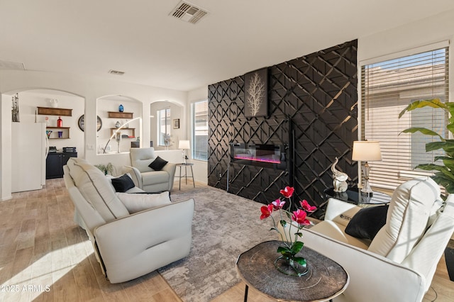 living room with arched walkways, visible vents, light wood-style floors, an accent wall, and a large fireplace