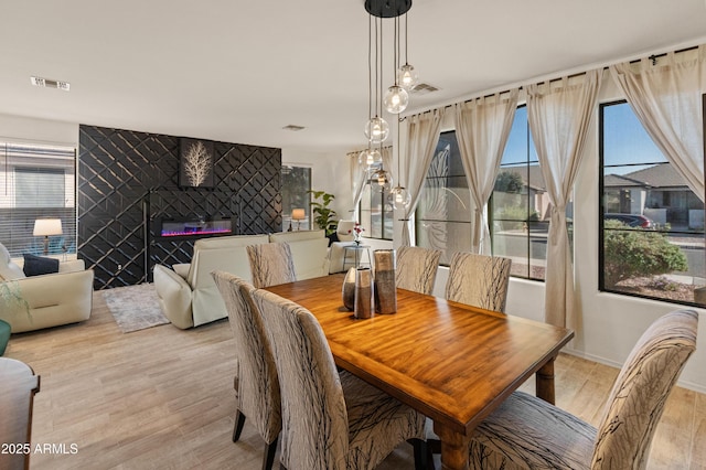 dining space featuring a fireplace, light wood finished floors, visible vents, an accent wall, and baseboards