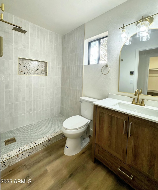 bathroom with a textured wall, a tile shower, vanity, toilet, and wood finished floors