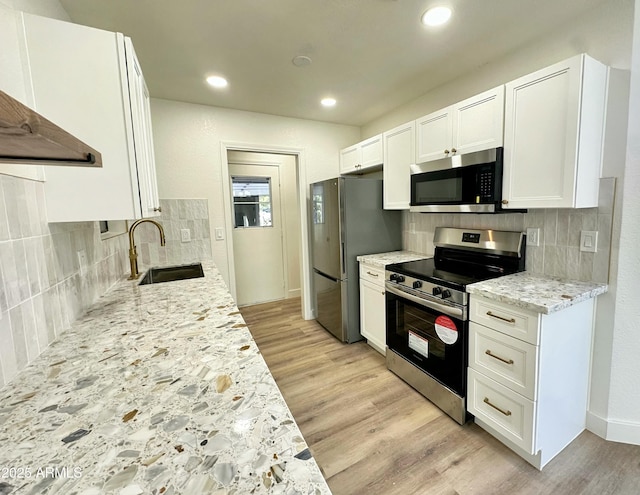 kitchen with decorative backsplash, white cabinetry, a sink, light wood-style flooring, and appliances with stainless steel finishes