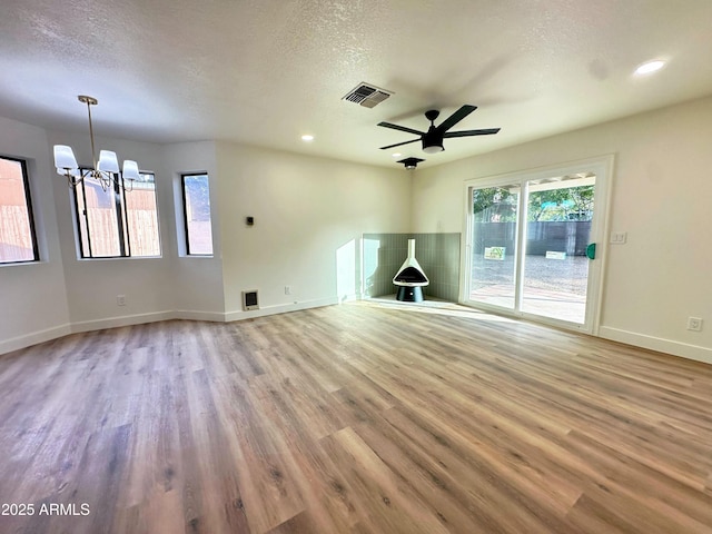 unfurnished living room with a textured ceiling, ceiling fan with notable chandelier, wood finished floors, and visible vents