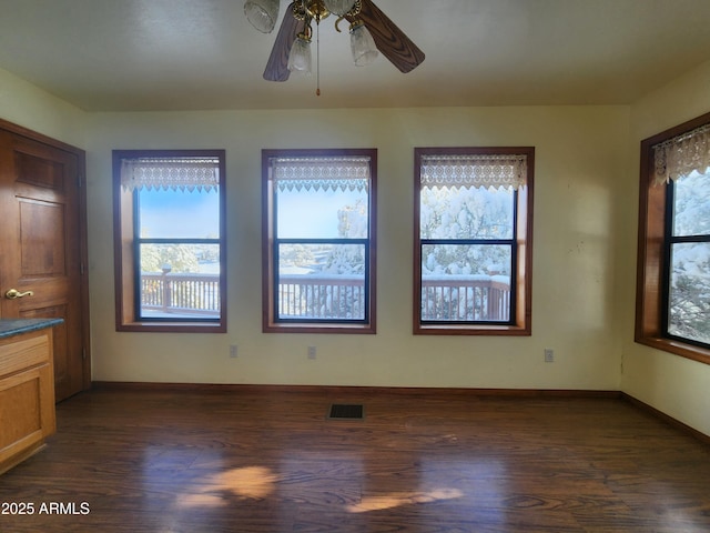 empty room with dark wood-type flooring, baseboards, visible vents, and ceiling fan