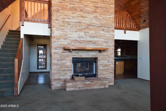 unfurnished living room featuring stairway, a fireplace, a high ceiling, and carpet