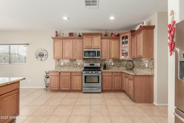 kitchen featuring backsplash, light stone countertops, stainless steel appliances, and light tile patterned floors