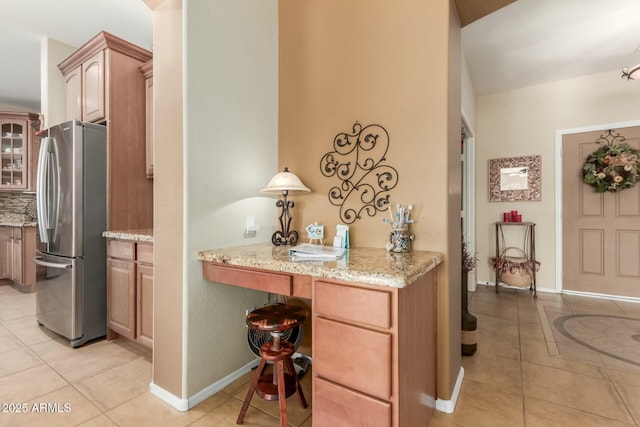 kitchen featuring stainless steel fridge, light stone counters, light tile patterned floors, and a breakfast bar area