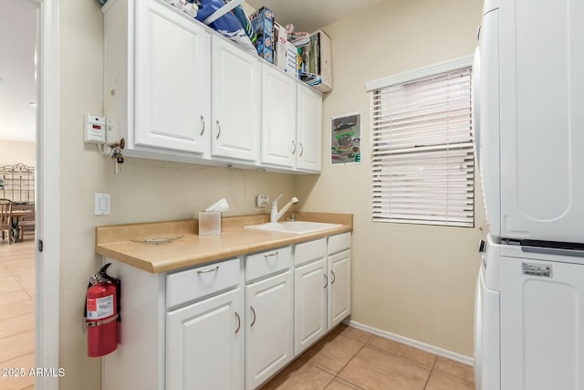 laundry room with light tile patterned flooring, stacked washer / dryer, cabinets, and sink