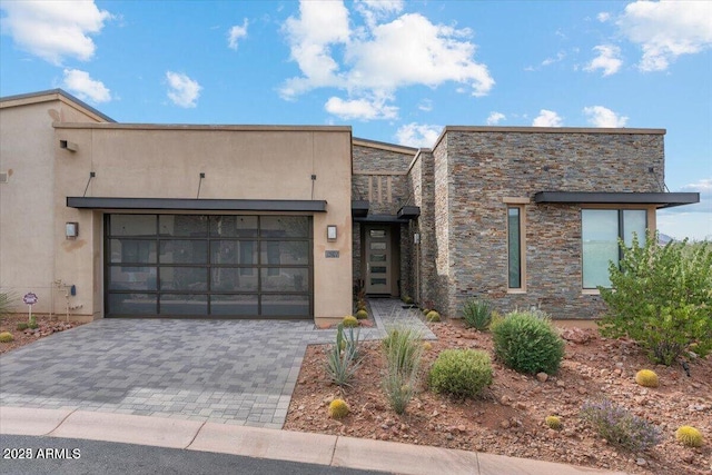 view of front of property with a garage, stone siding, decorative driveway, and stucco siding