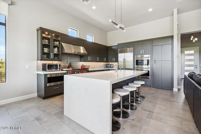 kitchen with decorative backsplash, appliances with stainless steel finishes, a breakfast bar, light countertops, and under cabinet range hood