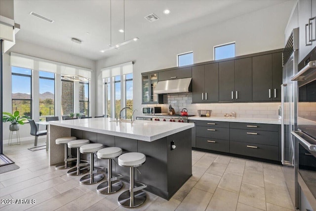 kitchen featuring tasteful backsplash, light countertops, visible vents, under cabinet range hood, and a kitchen bar