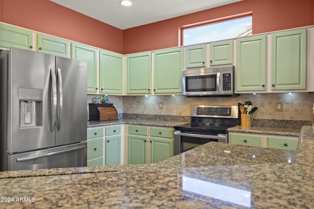 kitchen with tasteful backsplash, green cabinets, appliances with stainless steel finishes, and stone countertops