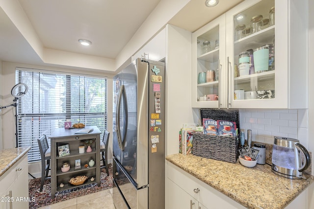 kitchen with light stone counters, white cabinetry, stainless steel refrigerator, and tasteful backsplash