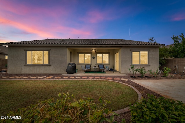 back house at dusk with a patio area, ceiling fan, and a lawn