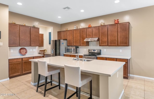 kitchen featuring light tile patterned flooring, sink, a center island with sink, appliances with stainless steel finishes, and a kitchen breakfast bar