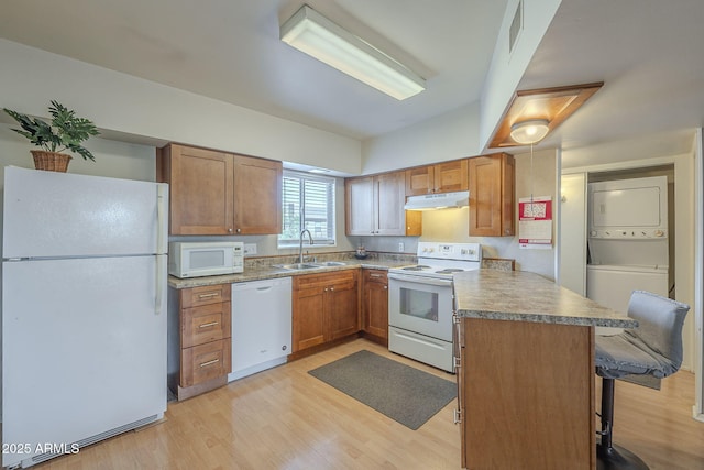 kitchen featuring stacked washer and clothes dryer, sink, a breakfast bar area, kitchen peninsula, and white appliances