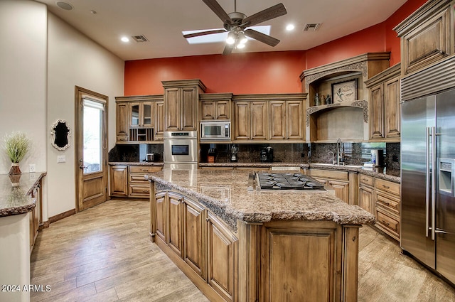 kitchen featuring a center island, built in appliances, backsplash, light wood-type flooring, and stone counters