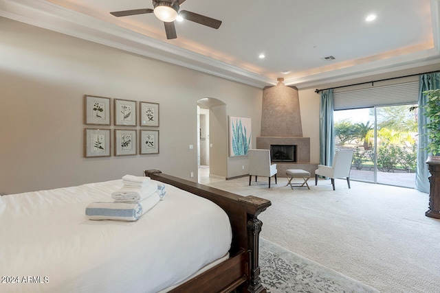 bedroom with ceiling fan, access to exterior, a raised ceiling, a large fireplace, and carpet flooring