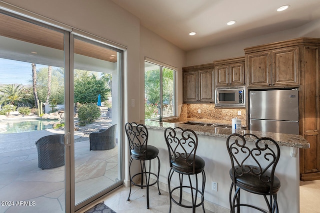 kitchen featuring a kitchen bar, kitchen peninsula, appliances with stainless steel finishes, tasteful backsplash, and light stone counters