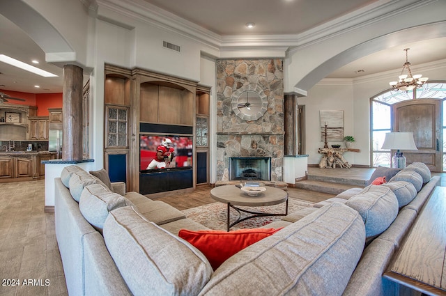 living room with light wood-type flooring, ceiling fan with notable chandelier, ornamental molding, and a fireplace