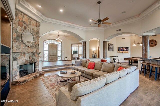 living room featuring a fireplace, ceiling fan with notable chandelier, crown molding, and hardwood / wood-style flooring